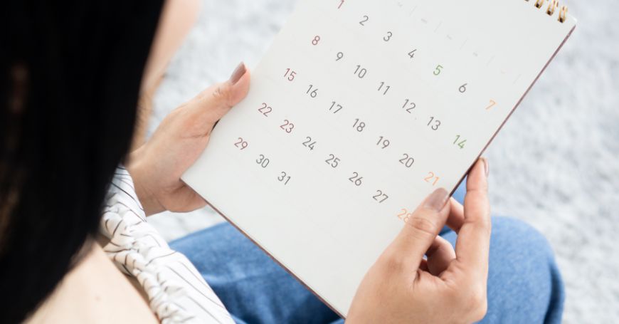 Person hält einen Kalender in der Hand, um den Zyklus zu überprüfen und zu entscheiden, ob natürliche Heilmittel verwendet werden sollen